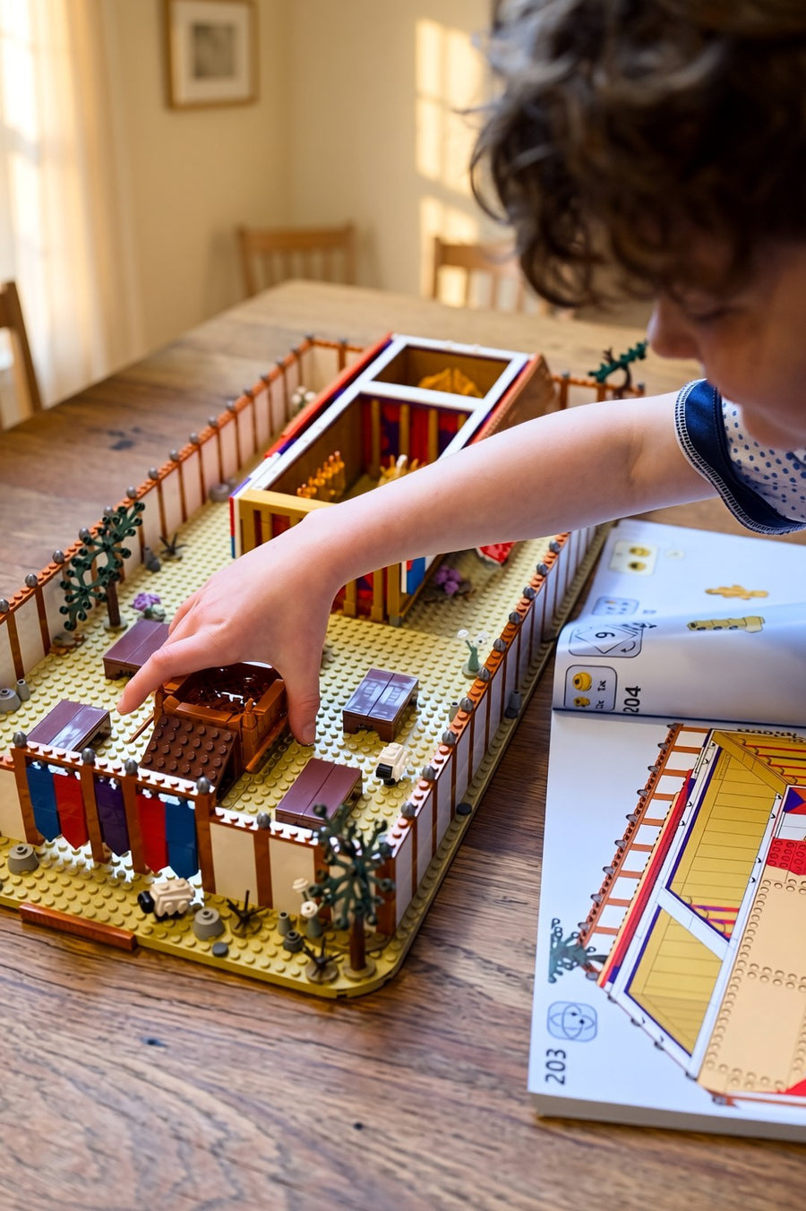 A child building the Tabernacle set with the instruction booklet at the family table